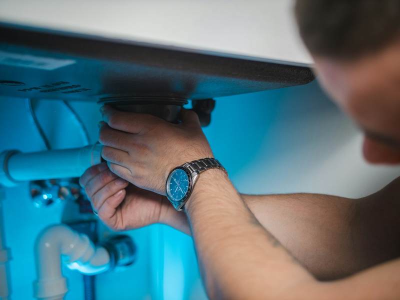 Plumber’s hands working on the drain pipes beneath a sink