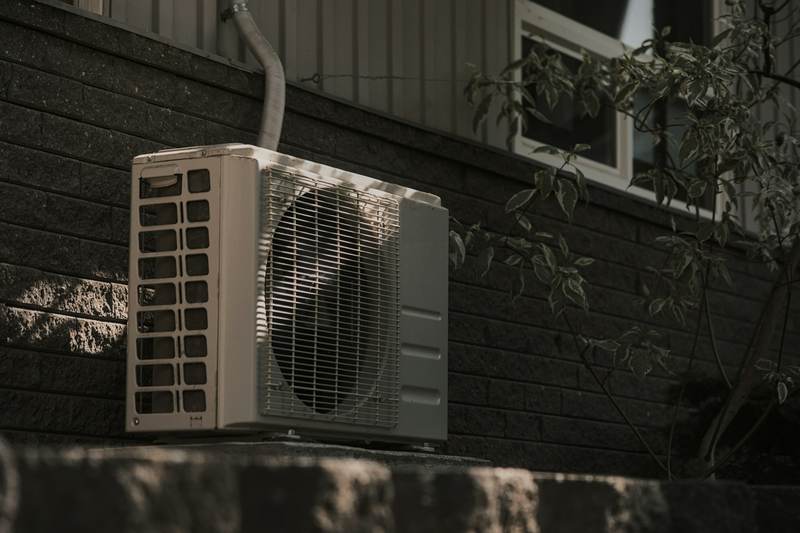 Ductless mini-split condenser mounted against a dark brick wall