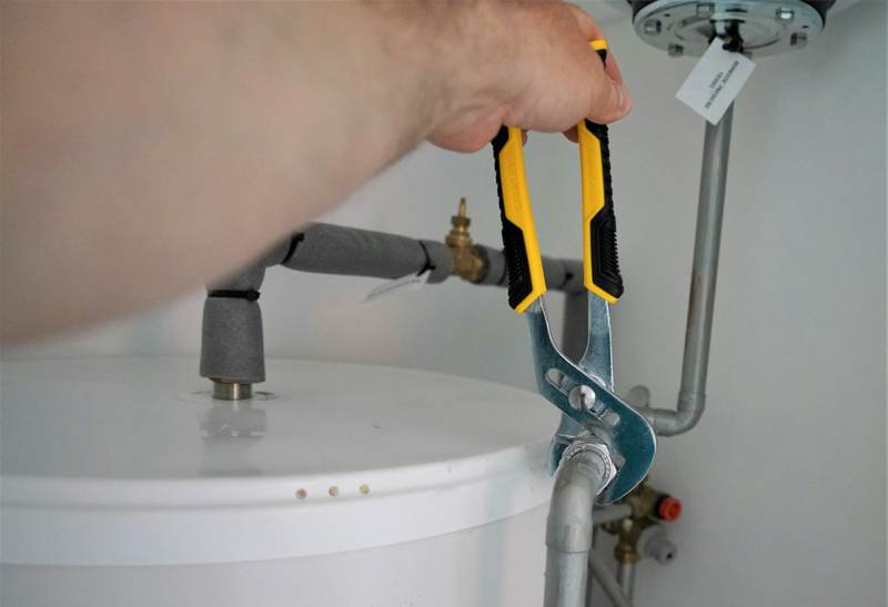 Plumber tightening a fitting on top of a residential water heater