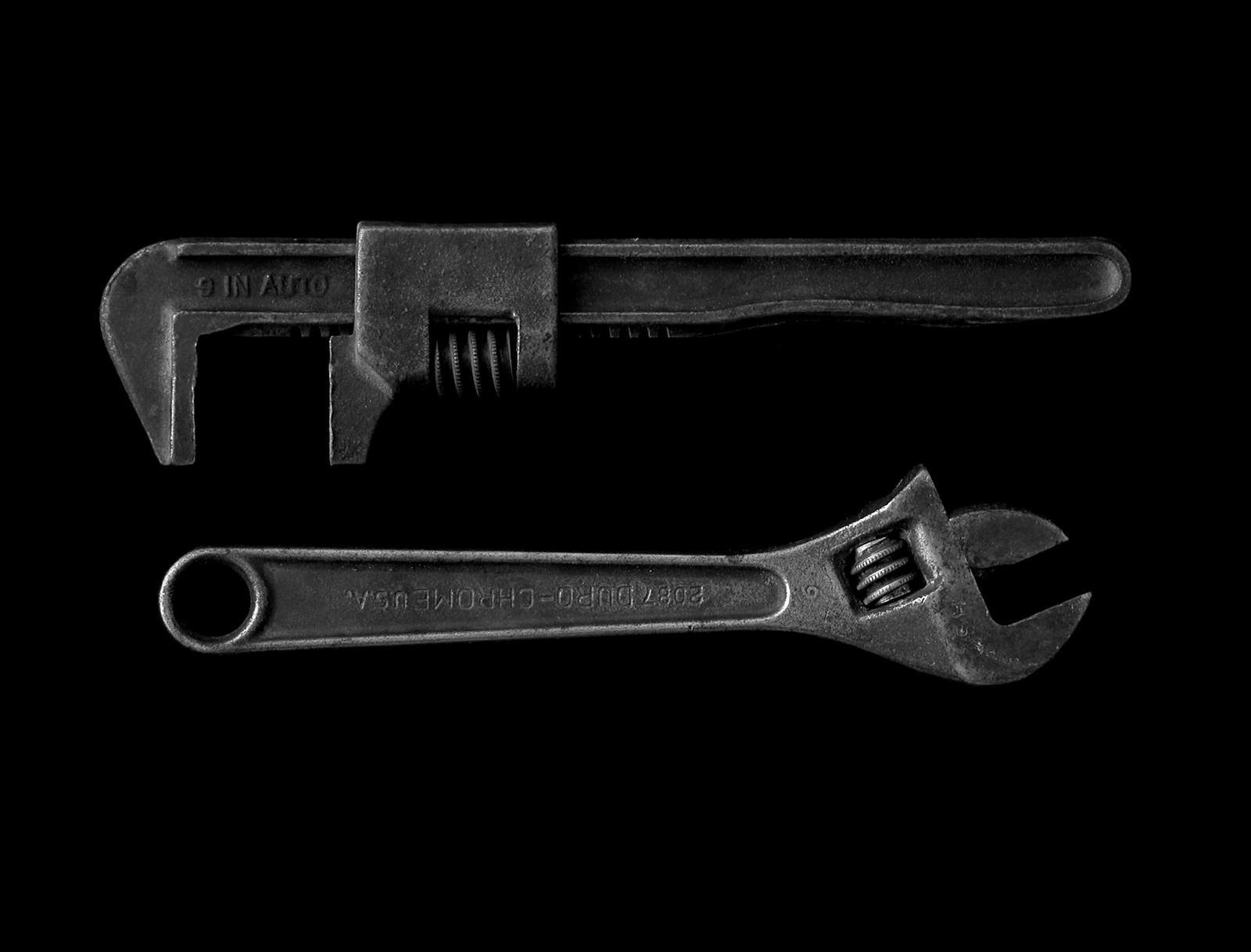 An old pipe wrench and an adjustable wrench on a black background